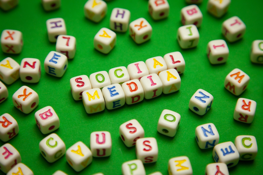 Green background with tiles that spell out social media together. They are surrounded by other tiles with various letters.